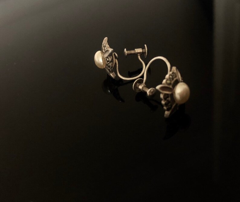 May include: A pair of silver clip-on earrings with a pearl and marcasite design.