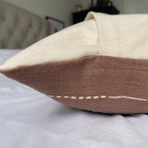 Pu&ograve; includere: Un cuscino marrone e bianco con un semplice design cucito. Il cuscino &egrave; realizzato in un tessuto morbido e testurizzato.