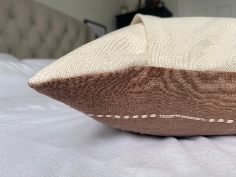 Pu&ograve; includere: Un cuscino marrone e bianco con un semplice design cucito. Il cuscino &egrave; realizzato in un tessuto morbido e testurizzato.