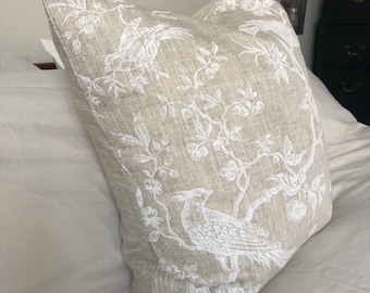 May include: A beige linen pillow with a white floral and bird design. The pillow is on a white bed.