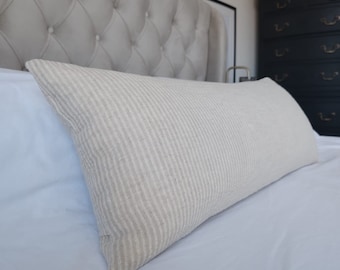 May include: A white bed with a gray tufted headboard and a white and beige striped lumbar pillow.