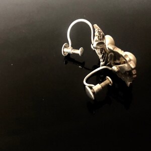 May include: A pair of silver clip-on earrings with a floral design. The earrings have a screw-back closure.