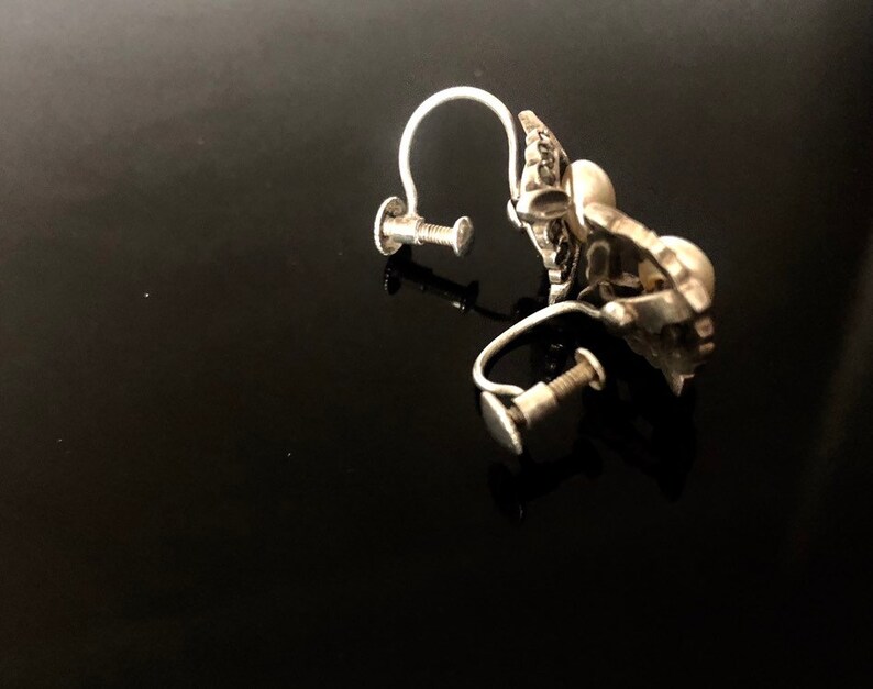 May include: A pair of silver clip-on earrings with a floral design. The earrings have a screw-back closure.