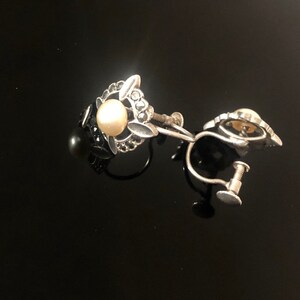 May include: A pair of silver clip-on earrings with a faux pearl and black stones.