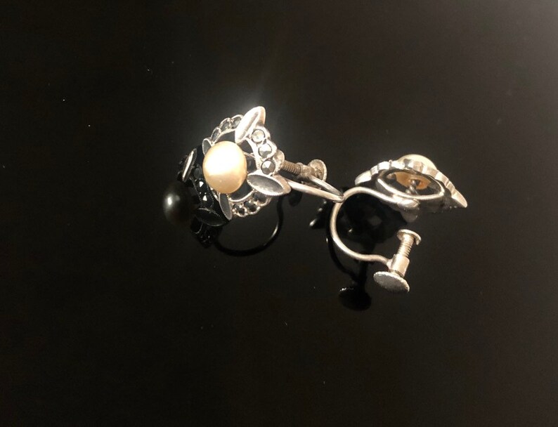 May include: A pair of silver clip-on earrings with a faux pearl and black stones.