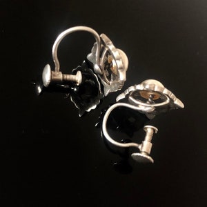 May include: A pair of silver clip-on earrings with a pearl-like center and a decorative design around the pearl.