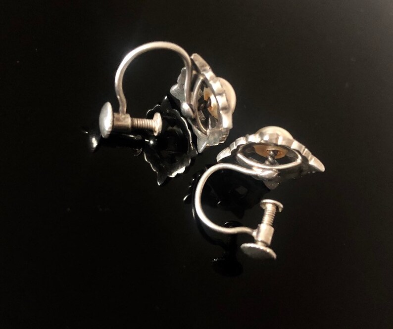 May include: A pair of silver clip-on earrings with a pearl-like center and a decorative design around the pearl.