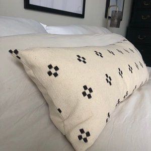 May include: A white pillow with a black geometric pattern. The pillow is on a white bed with white bedding.