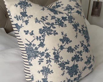 May include: A decorative pillow with a cream-colored background and a blue floral pattern. The pillow has a striped border on one side. The pillow is placed on a white bed.