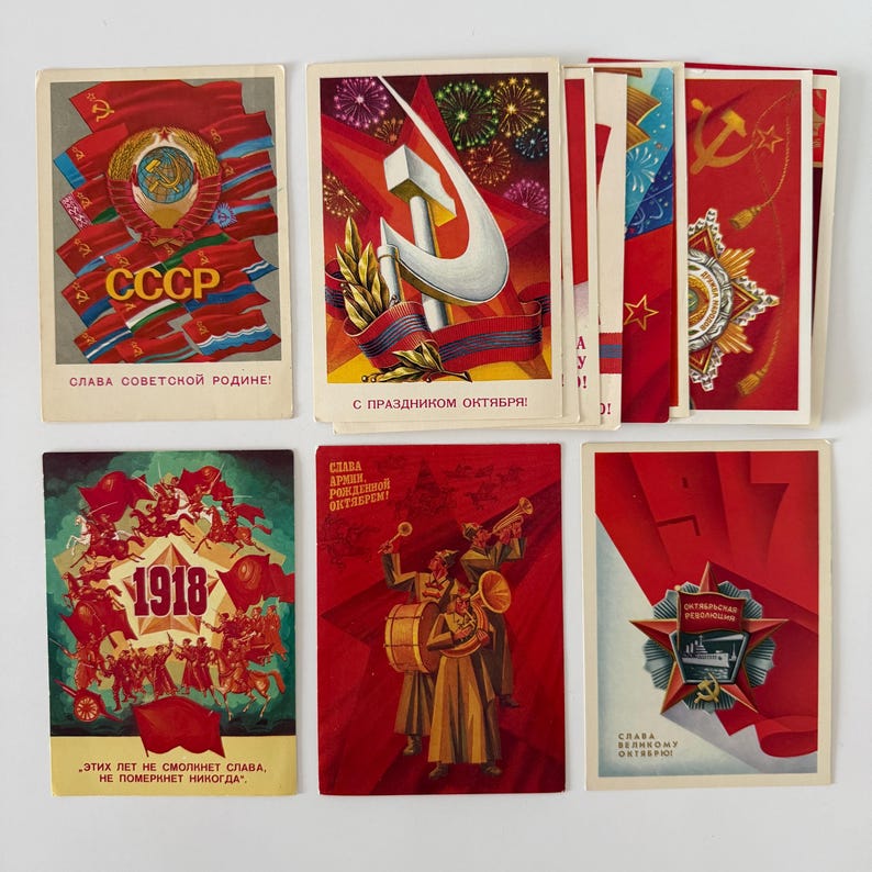 May include: A collection of six rectangular postcards featuring Soviet-themed illustrations in red, gold, and green. The designs include the hammer and sickle, military medals, marching musicians, and historical dates like 1918, with Cyrillic text printed on each.