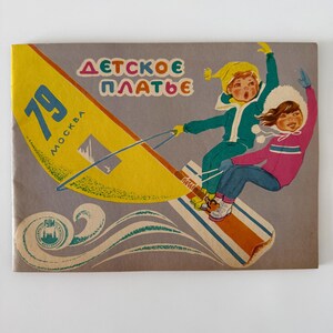May include: A vintage booklet cover featuring a yellow sail with the text 79 MOSKVA and the Cyrillic text DÉTSKOE PLÁT'E. Two children in winter clothing are depicted windsurfing on a board, with a circular logo in the bottom left corner.