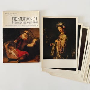 Op de afbeelding: Een verzameling kunstprints en een boek getiteld "Rembrandt Harmensz van Rijn". De boekomslag toont een schilderij van een vrouw en een baby. De kunstprints tonen klassieke schilderijen, waaronder een portret van een vrouw.