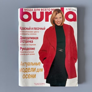 Puede incluir: Una portada de revista con una mujer con un abrigo rojo y un vestido negro. El título de la revista es "burda" en letras rojas grandes. El texto en ruso incluye "Modelos para otoño" y "Costura decorativa".