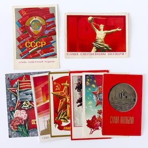 Könnte beinhalten: Eine Sammlung von Vintage-Propagandapostkarten aus der Sowjetzeit. Die Postkarten zeigen leuchtende Farben in Rot, Gold und Blau mit Bildern von Flaggen, Sternen und einer muskulösen Figur. Text auf Russisch ist auf mehreren Karten zu sehen.
