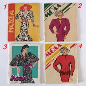 May include: Four vintage fashion magazines with illustrations of women's clothing. The covers feature bold colors and graphic designs. Each magazine has the word "Moda" or "MOAA" on the cover, with illustrations of women in stylish outfits.