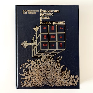 Pode incluir: Um livro de capa dura preto intitulado "Грамматика русского языка в иллюстрациях" de K.I. Pekhliyanova e M.N. Lebedeva. A capa apresenta um desenho de linha dourada de um cubo com uma chave, uma pequena abelha e um arranjo floral denso.