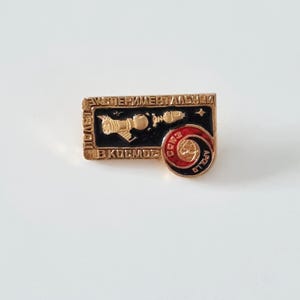 May include: A vintage gold-toned pin with a black background featuring a spacecraft design and Cyrillic text. The pin includes a red and gold circular emblem with the word "Apollo".