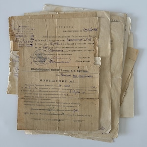 May include: A stack of aged, tan-colored papers with handwritten text, stamps, and official seals. The documents appear to be from an institute, with some text in a foreign language. The papers are slightly torn and worn, suggesting age.
