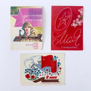 May include: Three vintage Soviet postcards. One shows a soldier with a star and text. Another is red with a star and the word "May". The third card has a flag, doves, and the date "9 May".
