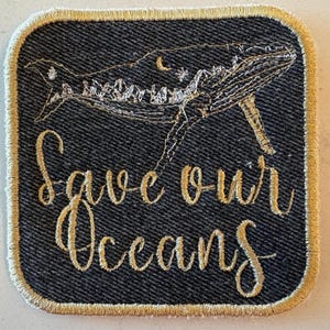 May include: Embroidered patch with a whale design and the words "Save our Oceans" in gold thread on a dark denim background. The patch has a gold border and a square shape with rounded corners.