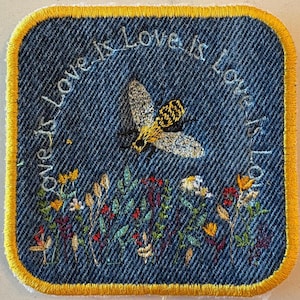 May include: Embroidered denim patch with a yellow border. The patch features a bee and wildflowers, with the words "Love is Love" arched across the top. The bee has yellow and black stripes.