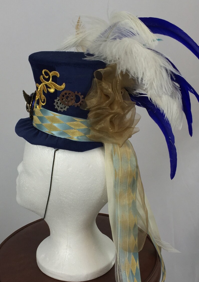 May include: A blue top hat with gold and silver embellishments, a gold and blue ribbon, a white and blue feather plume, and a gold tulle bow.
