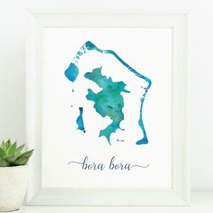 Könnte beinhalten: Ein Aquarellbild der Insel Bora Bora, mit dem Namen "bora bora" in Kursivschrift unterhalb der Insel. Das Bild ist in einem weißen Rahmen gerahmt und liegt auf einer weißen Oberfläche.
