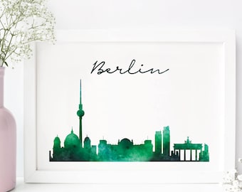 May include: A framed watercolor print of the Berlin skyline in shades of green. The word "Berlin" is written in cursive above the skyline. A pink vase with white flowers is to the left of the framed print.