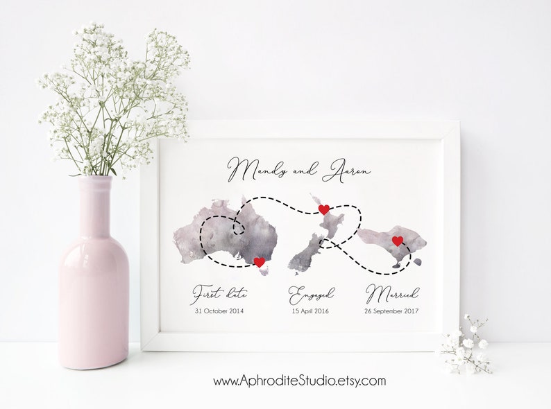 May include: A watercolor print of a map of Australia and New Zealand with a dashed line connecting three red hearts. The text "Mendy and Aaron" is at the top of the print. The text "First Date 31 October 2014", "Engaged 15 April 2016", and "Married 26 September 2017" is below the map. The text "www.AphroditeStudio.etsy.com" is at the bottom of the print.