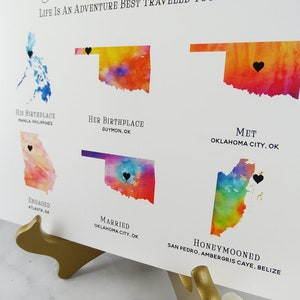May include: A watercolor map print showing the locations of a couple's life journey. The map shows their birthplaces, where they met, got engaged, married, and honeymooned. The text on the map reads "Life is an adventure best traveled together".