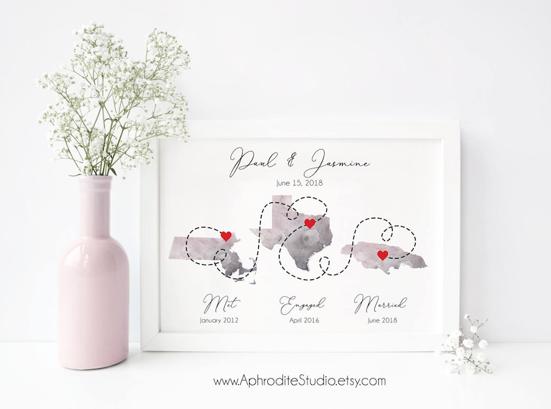 May include: A watercolor print of a map with a dotted line showing the journey of a couple's relationship. The map shows three locations with red hearts marking the spots where they met, got engaged, and married. The print includes the couple's names, "Paul & Jasmine", and the dates of each milestone. The text at the bottom of the print reads "www.AphroditeStudio.etsy.com".