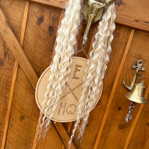 May include: A wooden sign with the text "The HQ" and a cross with the letter "E" on top. The sign is hanging on a wooden door with a gold hook and a gold bell.