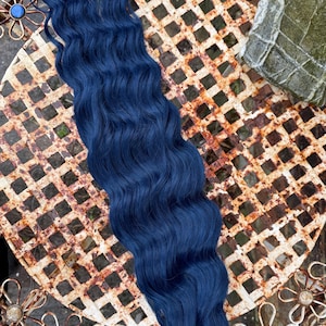 May include: A dark blue wavy hair extension. The hair is laid out on a rusty metal surface with a floral design.