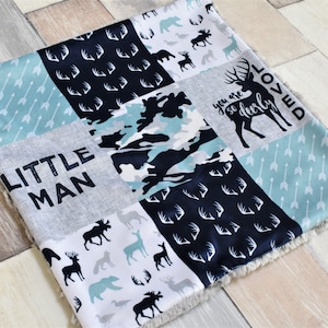 Puede incluir: Una manta de bebé de patchwork con un esquema de color azul, blanco y gris. La manta presenta una variedad de estampados de animales del bosque, incluidos ciervos, alces y osos. El texto "Little Man" y "You are so dearly loved" está impreso en la manta.