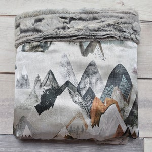 Puede incluir: Una bolsa de almacenamiento de tela gris y blanca con un ribete de piel sint&eacute;tica. La bolsa presenta un patr&oacute;n de cordillera en tonos grises, negros, marrones y azules.