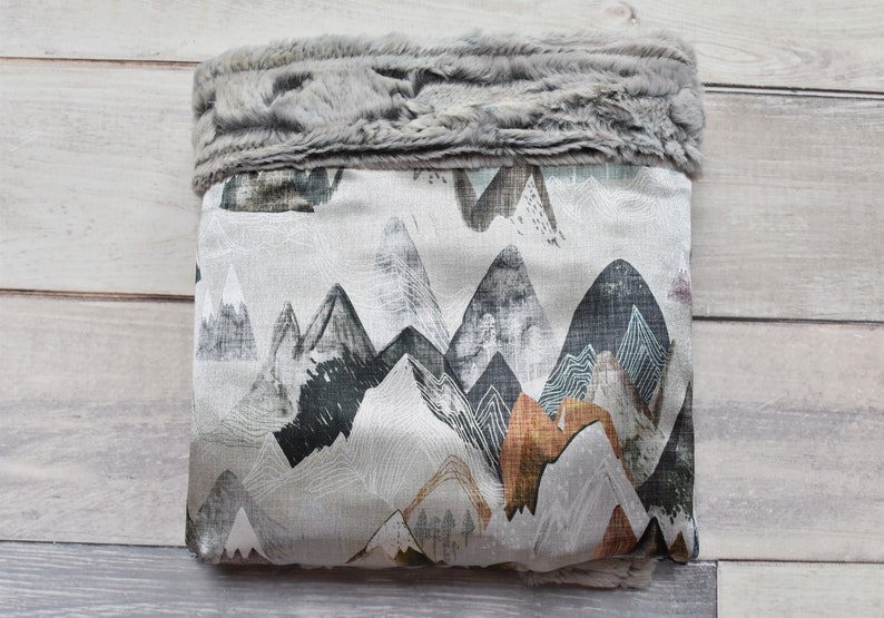 Puede incluir: Una bolsa de almacenamiento de tela gris y blanca con un ribete de piel sint&eacute;tica. La bolsa presenta un patr&oacute;n de cordillera en tonos grises, negros, marrones y azules.