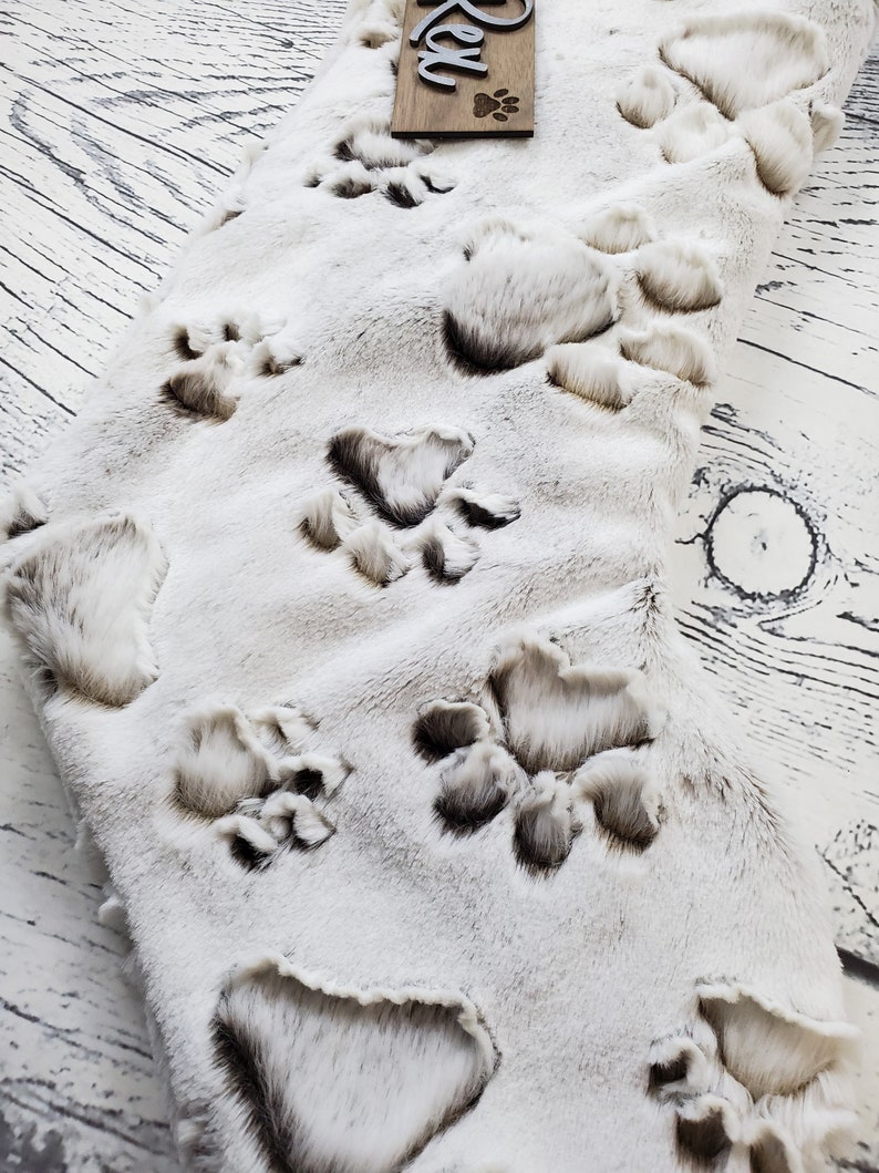 May include: White faux fur stocking with brown paw prints. The stocking has the name "Rex" on a wooden tag.