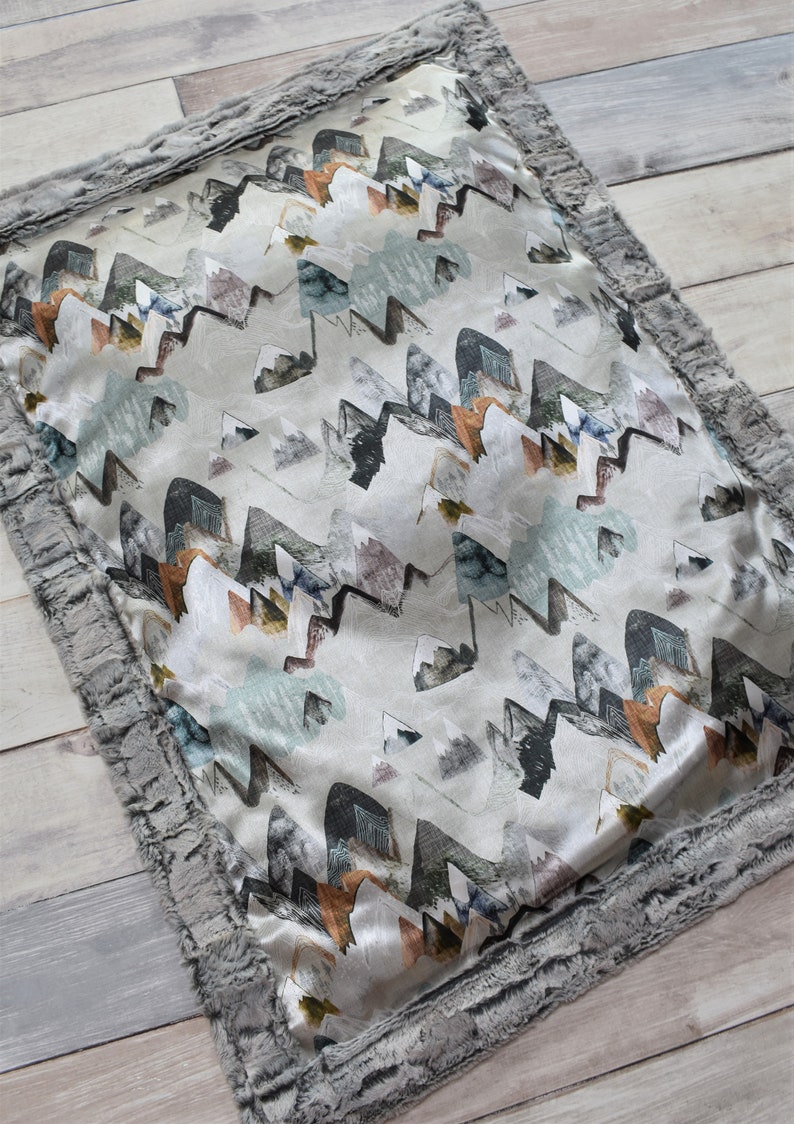 Puede incluir: Una almohada gris y blanca con un patr&oacute;n de formas abstractas en tonos grises, azules, verdes y naranjas. Tiene un ribete de piel sint&eacute;tica gris.