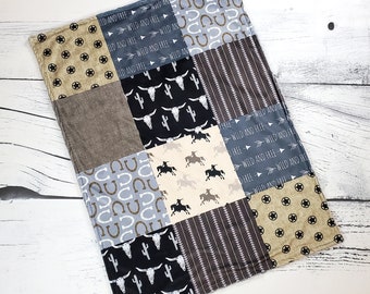 May include: A patchwork baby blanket with a western theme. The blanket is made of different fabrics with various patterns, including stars, horseshoes, cacti, and the words "Wild and Free".