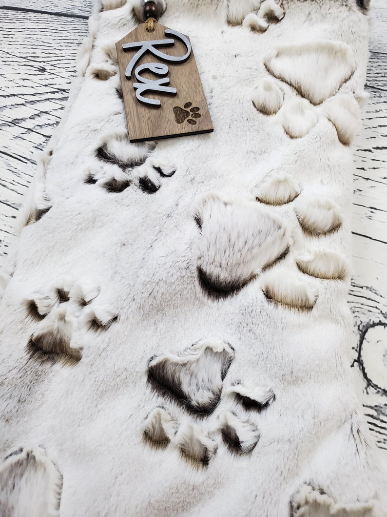 May include: White faux fur stocking with a brown wooden tag that says "Rex" and a paw print. The stocking is decorated with brown paw prints.
