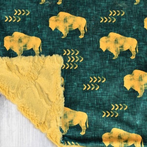 May include: A soft, plush blanket with a green and yellow buffalo print. One side of the blanket is a soft, fuzzy fabric, while the other side is a cotton fabric with a buffalo print.