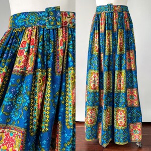 May include: A blue maxi skirt with a colorful patterned design. The skirt has a waistband with a buckle closure and a flowing silhouette.