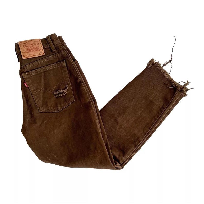 Puede incluir: Vaqueros de mezclilla marr&oacute;n con dobladillo deshilachado y un parche de Levi's en el bolsillo trasero.