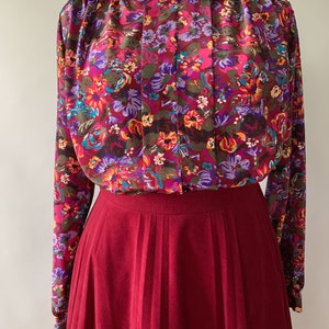 May include: A vintage floral print blouse with a burgundy pleated skirt. The blouse features a vibrant pattern of pink, purple, and orange flowers on a dark background. The skirt is a solid, deep red color.