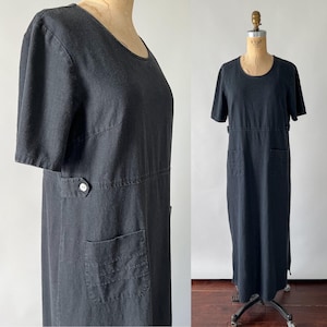 May include: A black linen dress with short sleeves, a round neckline, and two pockets. The dress has a simple, classic design.