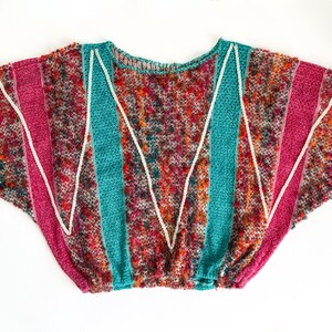 May include: A colorful, textured knit sweater with a round neckline. The sweater features vertical stripes of teal, pink, and tan, separated by white zigzag lines. The body of the sweater is a mix of red, orange, and brown.