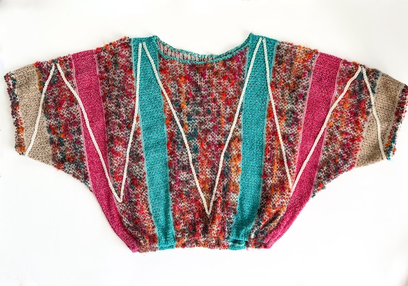 May include: A colorful, textured knit sweater with a round neckline. The sweater features vertical stripes of teal, pink, and tan, separated by white zigzag lines. The body of the sweater is a mix of red, orange, and brown.