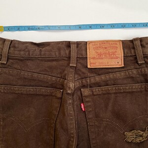 Puede incluir: Vaqueros de mezclilla marr&oacute;n con una etiqueta Levi's 550 en el bolsillo trasero. Los vaqueros tienen un aspecto desgastado con un peque&ntilde;o desgarro en el bolsillo trasero derecho.