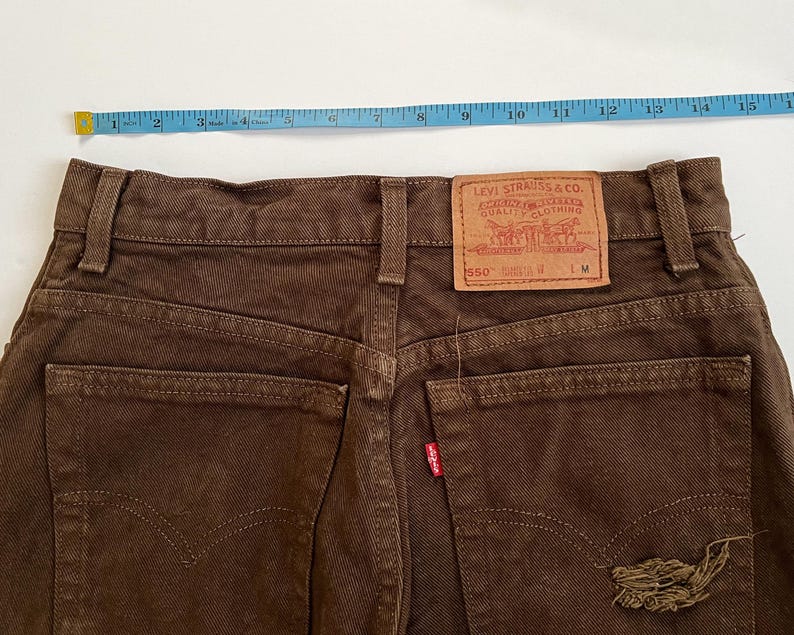 Puede incluir: Vaqueros de mezclilla marr&oacute;n con una etiqueta Levi's 550 en el bolsillo trasero. Los vaqueros tienen un aspecto desgastado con un peque&ntilde;o desgarro en el bolsillo trasero derecho.