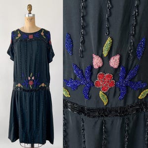 May include: Black vintage dress with short sleeves and a drop waist. The dress is adorned with colorful beaded floral designs and vertical beaded stripes. The neckline and hemline feature intricate beadwork, adding a touch of elegance to the garment.